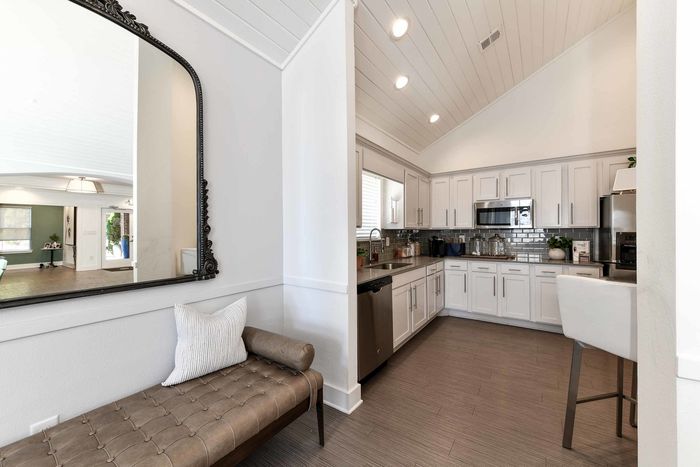 Elegant kitchen with white cabinets, stainless steel appliances, and modern backsplash, featuring a stylish mirror reflecting a spacious living area.