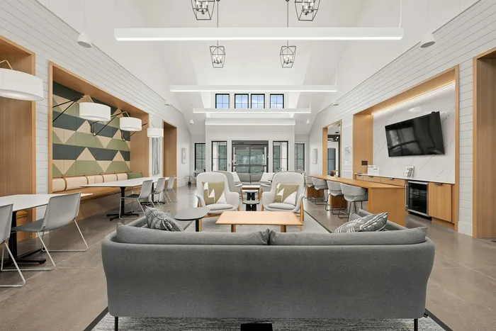Modern, spacious lounge area with sleek gray sofas, a stylish geometric accent wall, ample seating, and contemporary lighting fixtures.