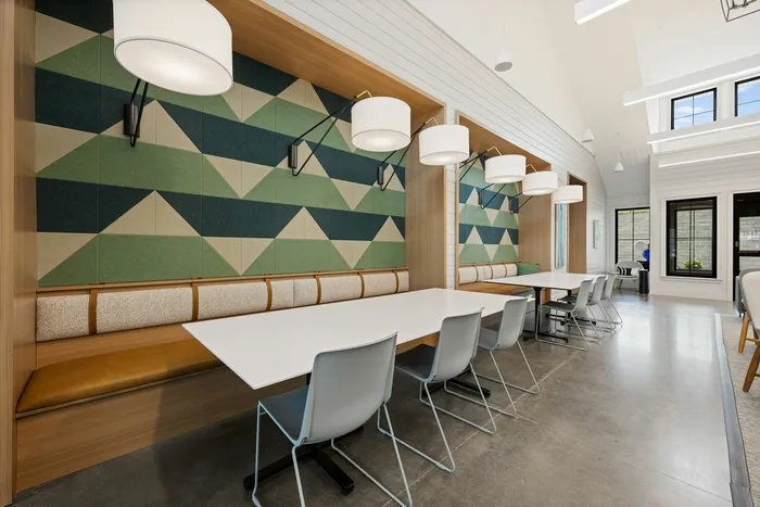 Modern communal dining area with geometric wall design, stylish pendant lighting, and sleek white tables surrounded by comfortable seating.