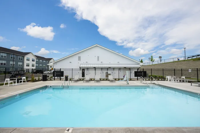 Inviting outdoor pool area with sleek white furnishings and a serene backdrop of modern apartments under a bright blue sky, perfect for relaxation and leisure.