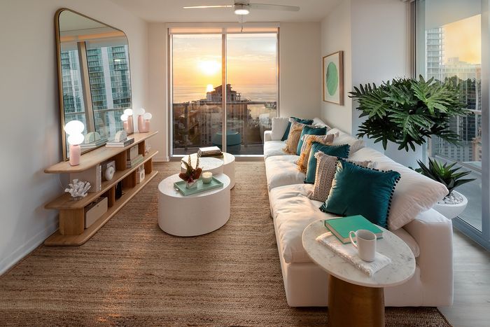 Elegant modern living room with a panoramic city view, featuring a cozy white sofa adorned with teal pillows, a chic oval coffee table, and stylish decor.