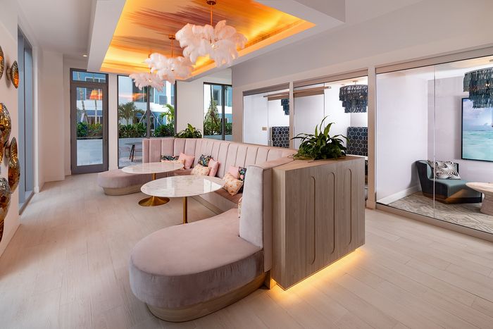 Luxurious lounge area with elegant pink seating, marble tables, and stunning feather chandeliers, illuminated by warm ambient lighting and framed by modern glass walls.