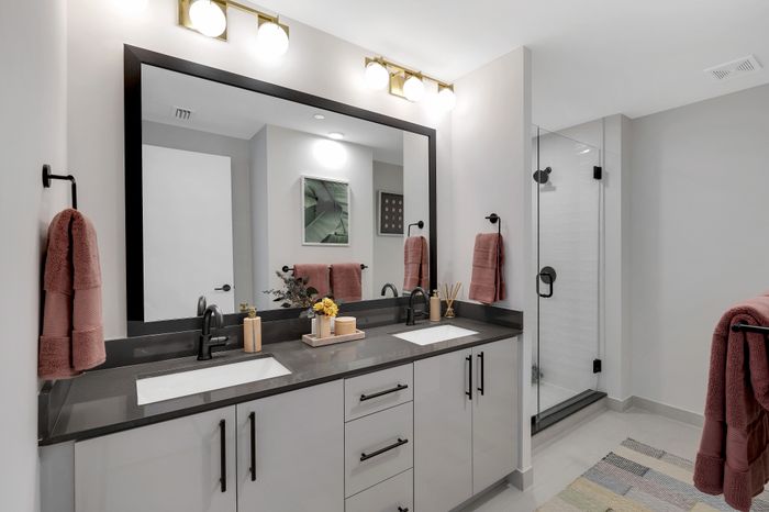 Elegant bathroom featuring a double vanity with sleek black fixtures, large mirror, and glass-enclosed shower. Soft pink towels and modern decor add a touch of sophistication.