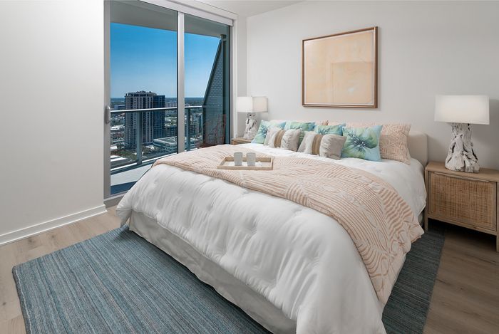 Luxurious bedroom with a cozy bed, vibrant cushions, modern decor, and stunning city views through floor-to-ceiling windows.