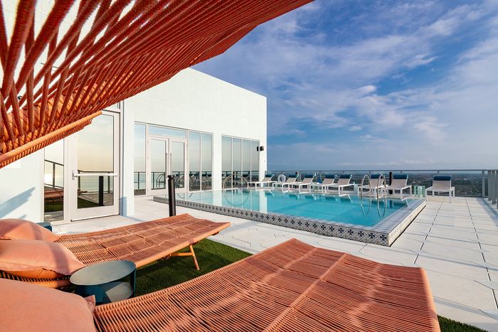 Luxurious rooftop pool area with modern sun loungers, expansive skyline views, and inviting blue skies.