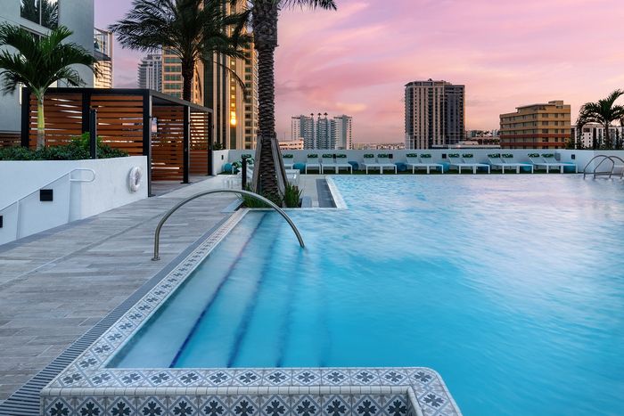 Luxurious rooftop pool area at sunset featuring elegant tile design, palm trees, and modern cityscape views.
