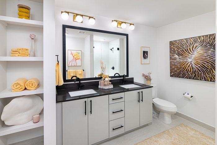 Elegant modern bathroom featuring a double vanity with sleek black fittings, illuminated by chic lighting. Decorated with luxurious yellow accents and artistic wall decor.
