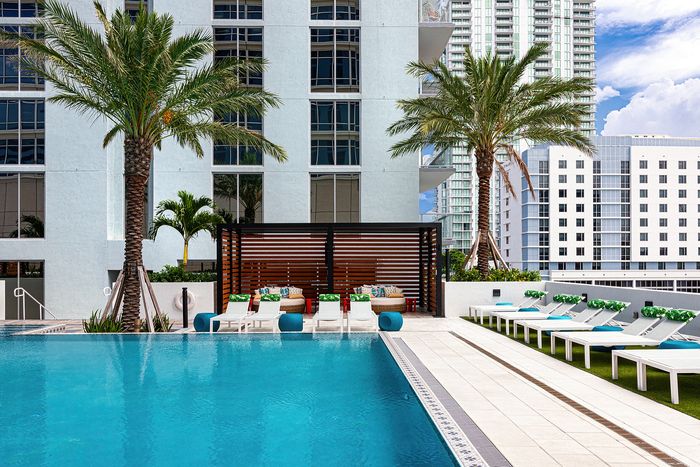 Luxurious urban oasis featuring a sparkling pool, elegant poolside lounge chairs, and lush palm trees, set against a backdrop of modern high-rise architecture.