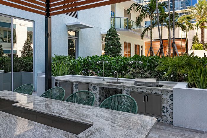Elegant outdoor kitchen area with modern grill, stylish stone countertops, and lush greenery in a chic apartment setting.