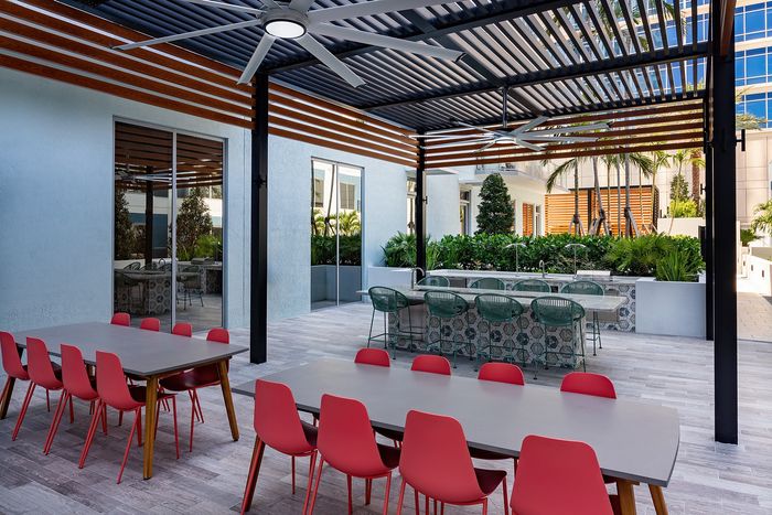 Chic outdoor terrace featuring modern dining tables with vibrant red chairs, a stylish pergola, and lush greenery, perfect for entertaining or relaxation.