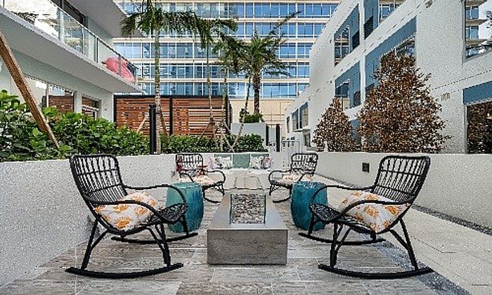 Chic outdoor seating area with stylish lounge chairs, vibrant cushions, and modern fire pit, surrounded by lush greenery and contemporary architecture.