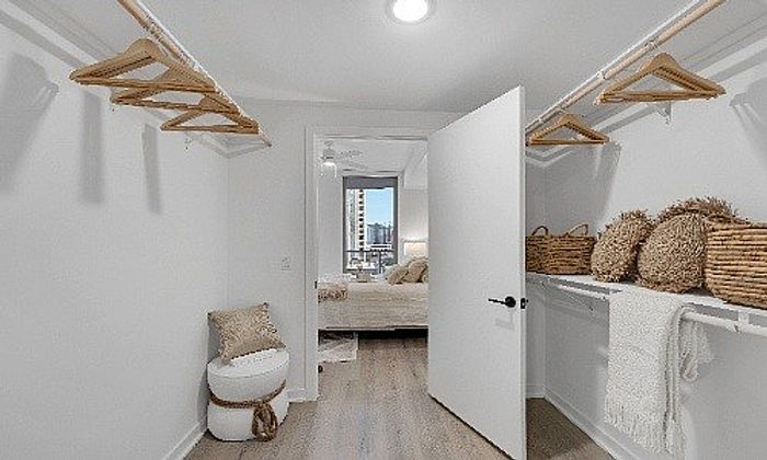 Chic walk-in closet with elegant wooden hangers and woven baskets leading to a cozy bedroom with a city view.