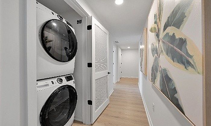 Modern apartment hallway featuring a stylish stacked washer and dryer, elegant wooden flooring, and contemporary wall art.
