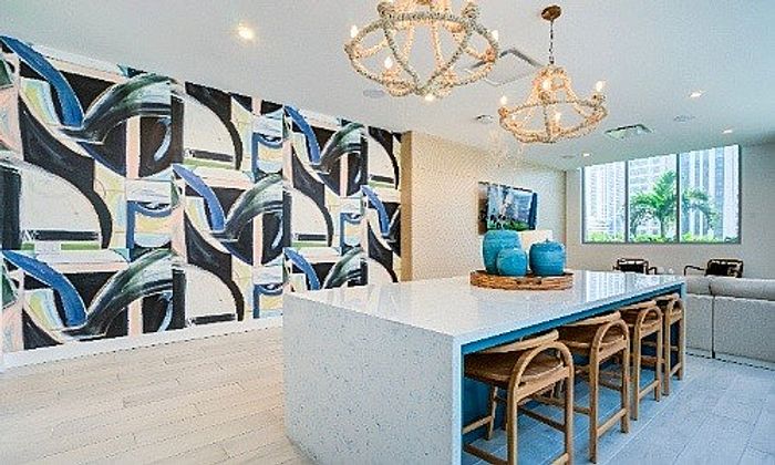 Contemporary living space with vibrant abstract wall art, elegant chandeliers, and a sleek white kitchen island with chic bar stools.
