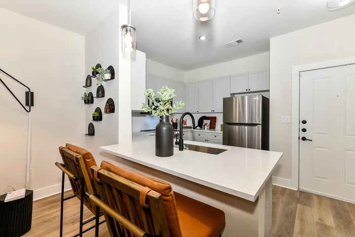 Chic modern kitchen with sleek white cabinetry, elegant countertops, and stainless steel appliances, accented by stylish pendant lighting and cozy bar seating.