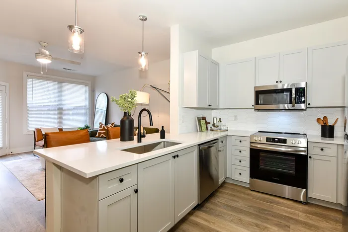 Modern apartment kitchen with sleek white cabinetry, stainless steel appliances, and a cozy open layout leading to a bright living area.
