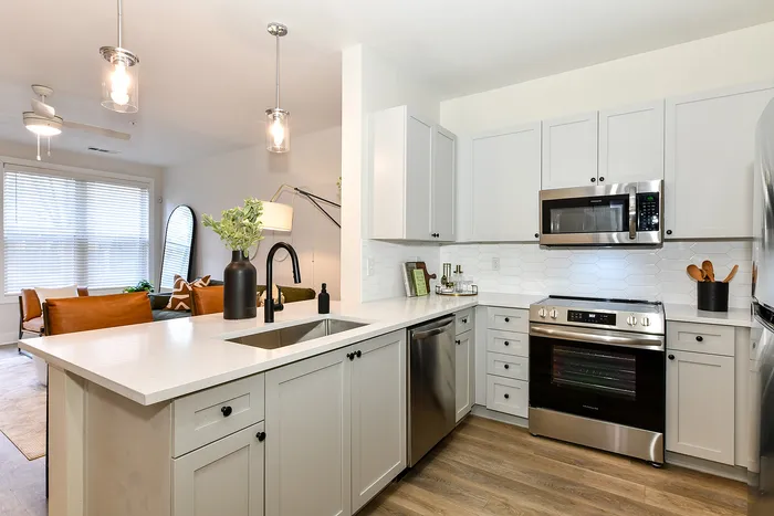Modern kitchen with stainless steel appliances, elegant pendant lighting, and open layout leading to a cozy living room featuring stylish leather seating.