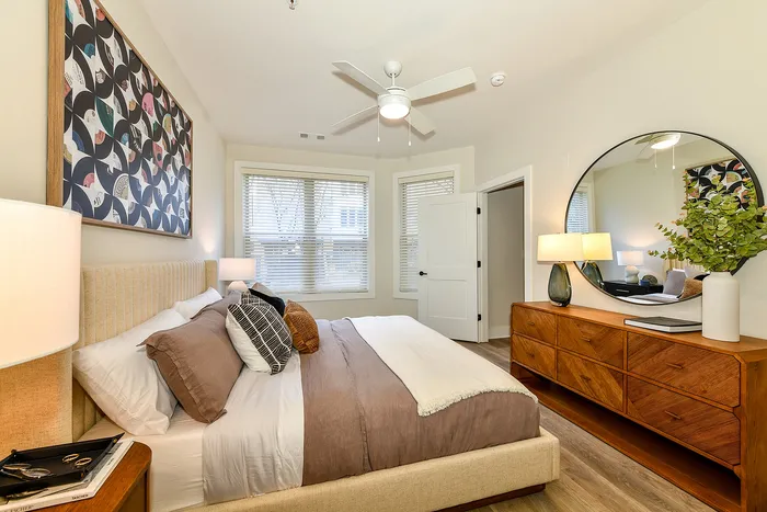 Inviting bedroom with modern decor, a plush bed adorned with cozy pillows, and a large circular mirror above a stylish wooden dresser.