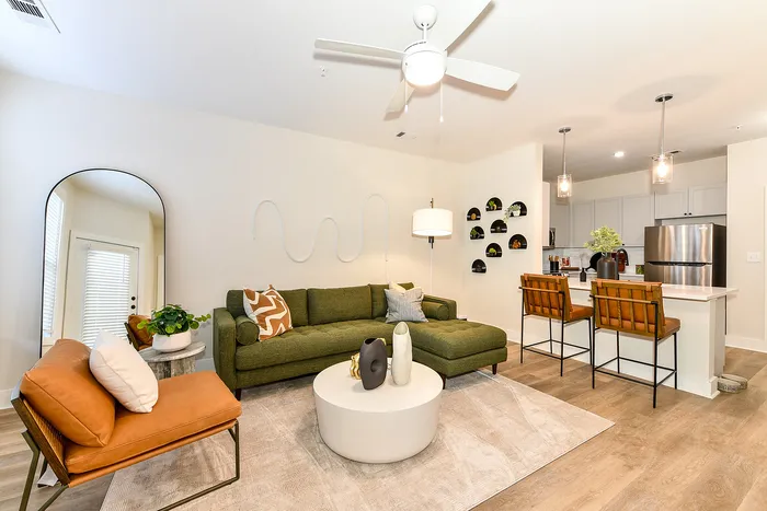 Chic open-concept living room with modern green sectional, stylish accents, and sleek kitchen with island seating.