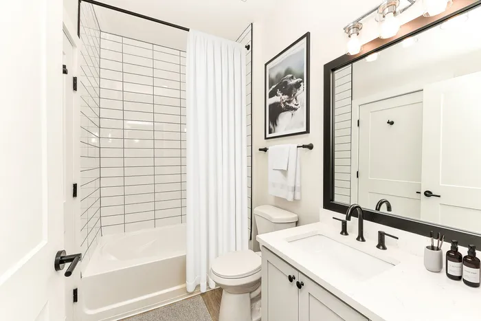 Elegant bathroom featuring a modern white vanity with black fixtures, a sleek mirror, and a stylish tiled shower.
