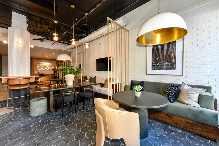 Modern apartment lounge with stylish leather chairs, sleek black dining table, and cozy sofa area, featuring hexagon tile flooring and contemporary lighting.