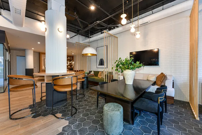Modern apartment lounge with stylish leather chairs, sleek black dining table, and cozy sofa area, featuring hexagon tile flooring and contemporary lighting.