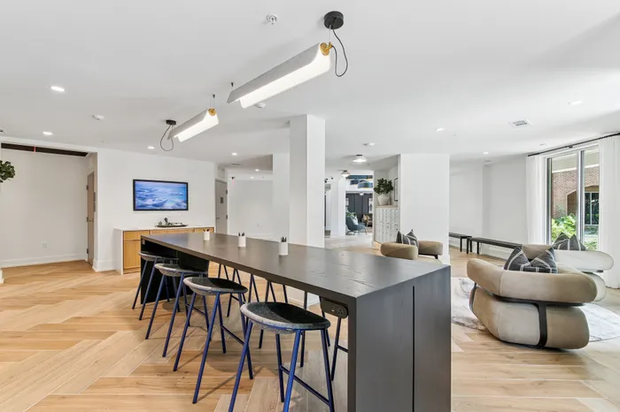 Modern communal space with sleek wooden flooring, stylish bar seating, and cozy lounge chairs, radiating contemporary elegance.