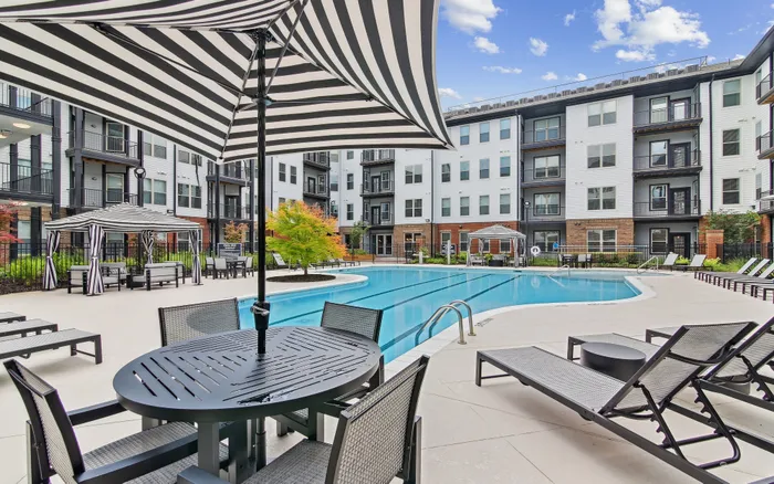 Luxurious apartment complex featuring a sparkling outdoor pool, stylish cabanas, and sleek modern architecture under a clear blue sky.