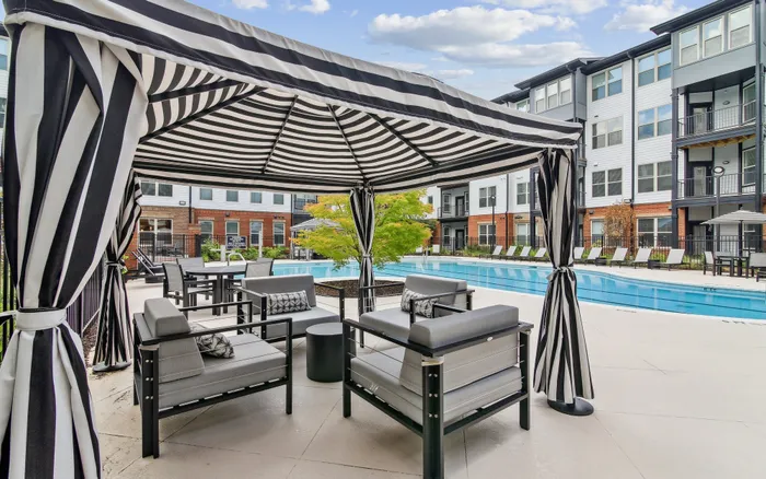 Luxurious apartment complex featuring a chic striped cabana and inviting poolside seating, perfect for relaxation.
