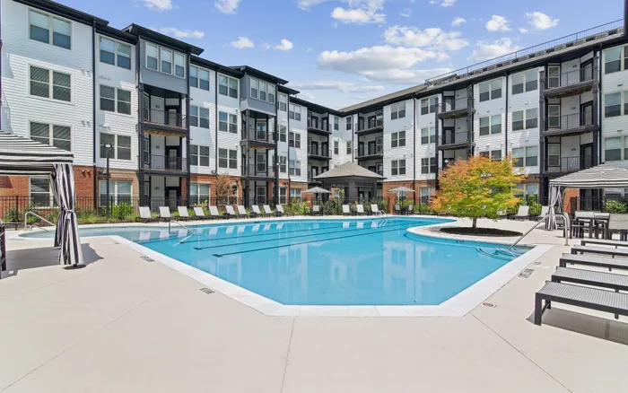Modern apartment complex with a luxurious swimming pool surrounded by stylish lounge chairs and vibrant landscaping.