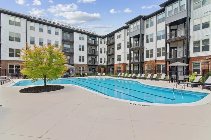 Modern apartment complex featuring a sparkling pool surrounded by comfortable lounge chairs and vibrant greenery, perfect for relaxation.