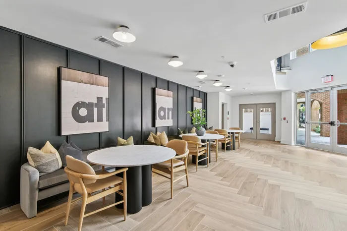 Modern communal lounge area with elegant marble tables, stylish wooden chairs, and cozy seating accented by artistic wall decor.