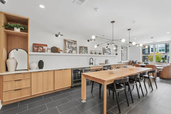 Sleek modern kitchen and dining area with stylish wood cabinetry, elegant shelving, and artistic lighting fixtures, leading to a bright and inviting living space with large windows.