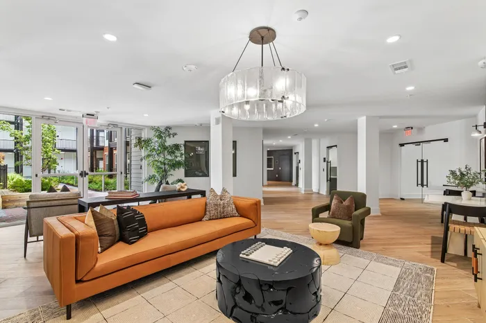 Elegant apartment lounge with a modern chandelier, stylish leather sofa, and a scenic view through large windows.