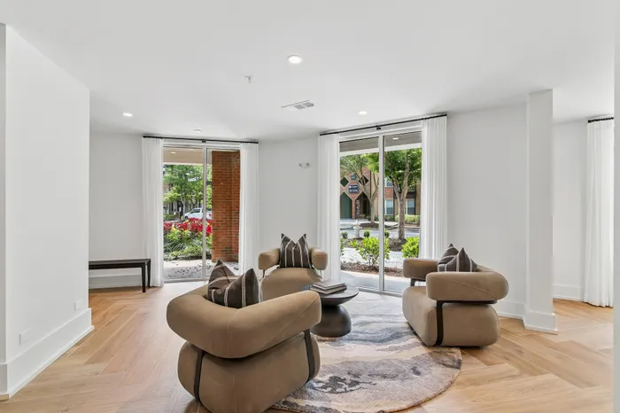 Elegant living room with plush brown armchairs, modern decor, and expansive windows offering a lush garden view.