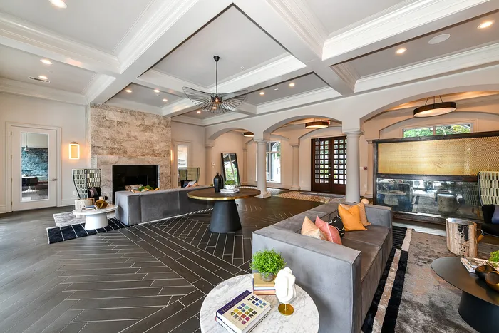 Elegant living room with modern decor, featuring a cozy gray sofa, chic lighting, and a stylish stone fireplace in an open-concept space.