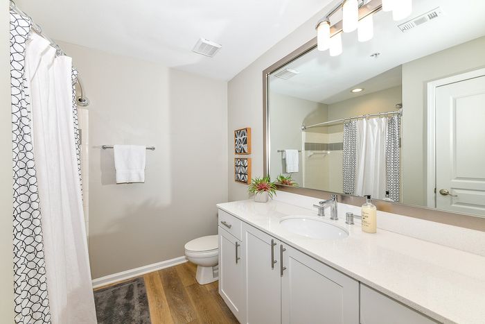 Bright and modern bathroom featuring sleek white cabinetry, elegant fixtures, and stylish decor with wood flooring.