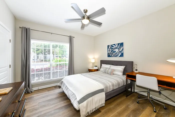 Bright and cozy bedroom with large window, stylish decor, and a modern wood desk, perfect for work or relaxation.