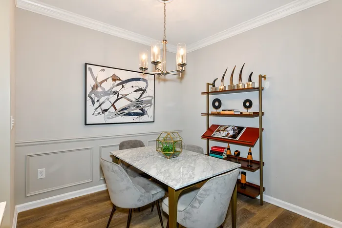 Elegant dining area with a marble-top table, plush chairs, modern chandelier, abstract art, and stylish shelving unit.