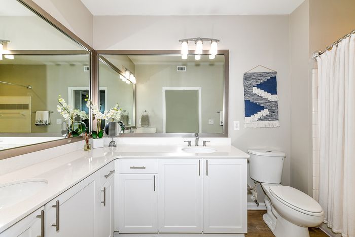 Modern and elegant bathroom with sleek white cabinets, large mirror, and tasteful decor.