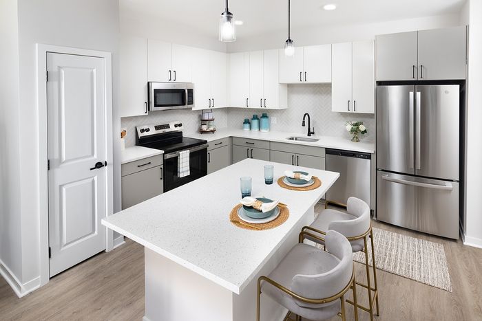 Modern apartment kitchen with white cabinetry, stainless steel appliances, and a spacious island with seating.