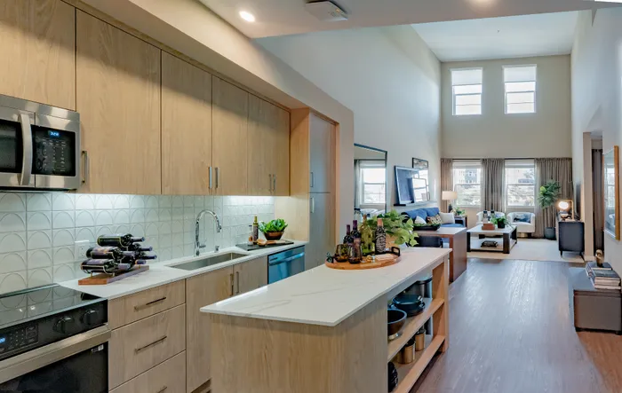 Modern open kitchen with sleek cabinetry, chic decor, and a bright living room featuring high ceilings and abundant natural light.