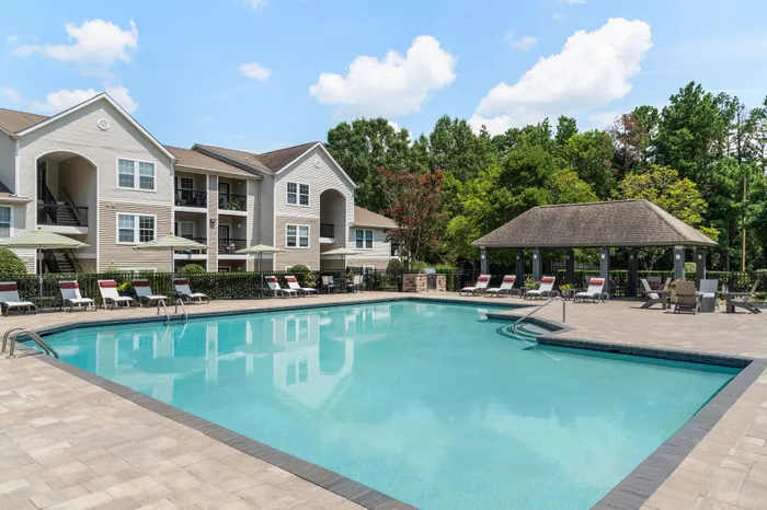 Charming apartment complex with luxurious outdoor pool and sunlit patio area, surrounded by lush greenery.