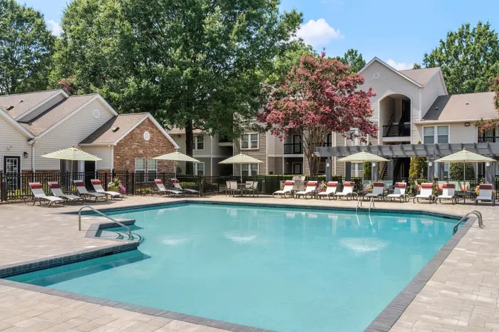 Luxurious apartment complex featuring a serene outdoor pool area with sun loungers, umbrellas, and lush landscaping against stylish residential buildings.