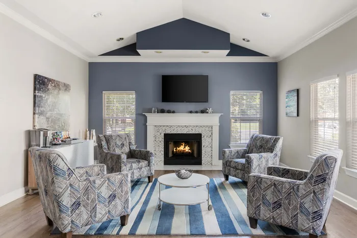 Chic living room showcasing cozy armchairs, a stylish fireplace, and a modern TV, set against a soothing blue accent wall with ample natural light filtering through large windows.