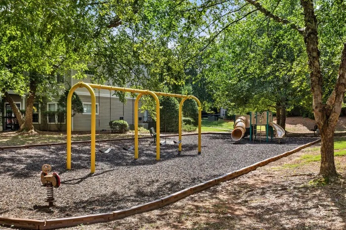 Charming community playground with swings, slide, and lush green surroundings, perfect for family fun.