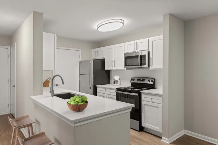 Modern kitchen with sleek white cabinetry, stainless steel appliances, and a cozy breakfast bar adorned with fresh green apples.