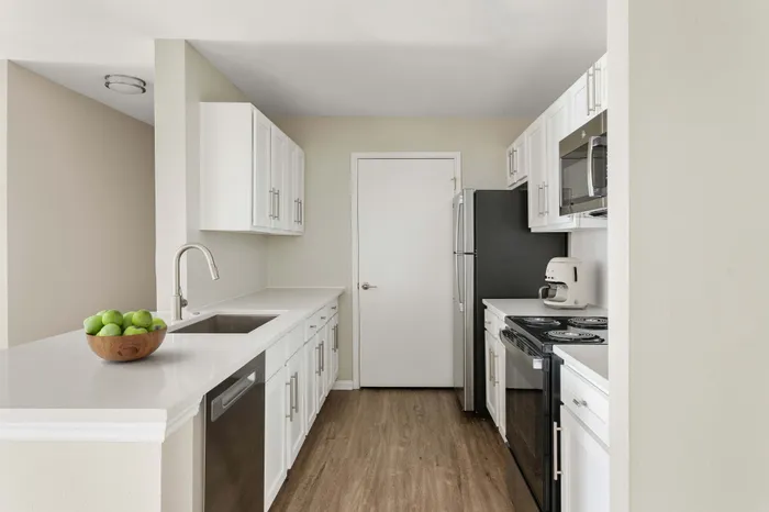 Modern kitchen featuring sleek white cabinetry, stainless steel appliances, and elegant countertops, complemented by a wooden bowl of green apples.