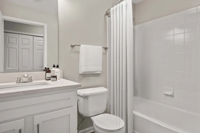 Modern bathroom with elegant white fixtures, sleek countertop, and stylish shower curtain offering a serene and clean atmosphere.