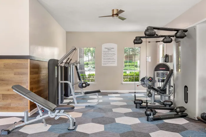 Inviting fitness center with modern exercise equipment, stylish geometric flooring, and large windows offering natural light.